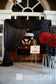 the entrance to an event with black drapes and red flowers in vases on display