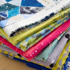 a pile of different colored fabrics sitting on top of a wooden table next to each other