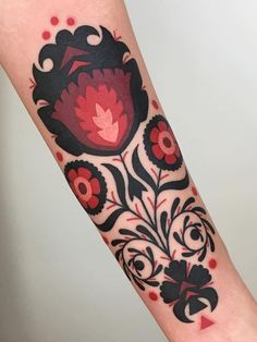 a red and black flower tattoo on the left arm with dots around it's edges