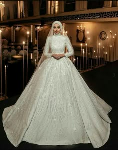 a woman in a white wedding dress standing next to some candles and looking at the camera