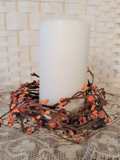 a white candle sitting on top of a table covered in branches and orange berries next to a wall