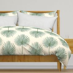 a bed with white pillows and green palm leaves on the comforter, along with two pillow cases