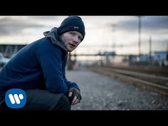 a man sitting on top of a bench next to train tracks with his hands in his pockets