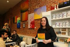 a woman standing in front of a table holding up a box with an orange and yellow painting on it