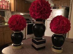 three black vases with red flowers on top of a table in front of a stove