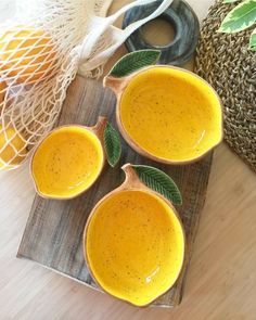 three yellow bowls with green leaves sit on a cutting board