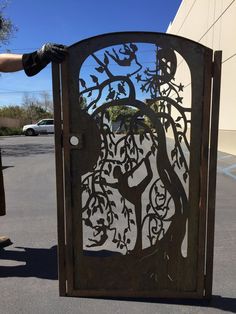 a person is holding up a metal gate with a tree design on the front and side