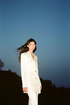 a woman in a white suit is standing on the ground with her hair blowing in the wind