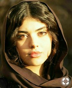 a woman wearing a brown shawl looking into the distance with her eyes wide open