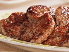 two pieces of meat sitting on top of a white and green plate next to a fork