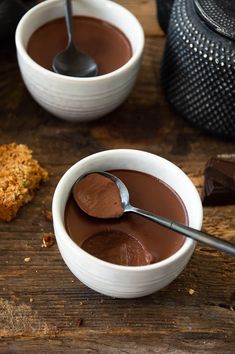 two white bowls filled with chocolate pudding on top of a wooden table next to a cookie