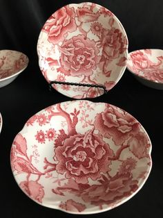 four red and white plates sitting on top of a black cloth covered table with flowers painted on them