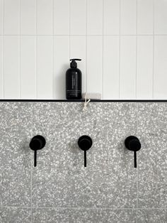 four black soap dispensers mounted to the wall next to a white tiled wall