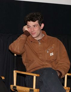 a young man sitting in a chair with his hand on his head and looking at the camera