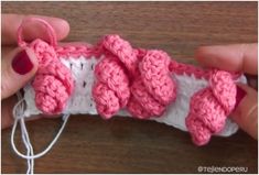 someone is crocheting some pink flowers on a piece of fabric