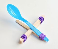 two toothbrushes sitting on top of each other next to a blue spoon with purple handles