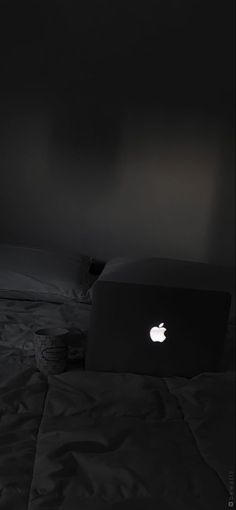 an apple laptop sitting on top of a bed in a room with black walls and white sheets