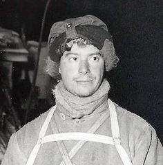 black and white photograph of a man wearing an apron with a hat on his head