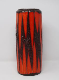 an orange and black vase sitting on top of a white table