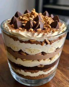 a layered dessert in a glass dish on top of a wooden table with nuts and chocolate