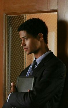 a young man in a suit and tie holding an ipad computer while standing next to a wooden door