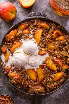 a skillet filled with fruit and ice cream on top of a table next to sliced peaches