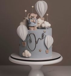 a blue cake decorated with hot air balloons and a teddy bear sitting on the top