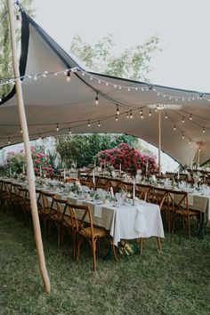 an outdoor tent with tables and chairs set up for a wedding reception under string lights