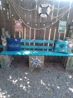 a blue bench sitting next to a wooden fence with decorative pillows on top of it