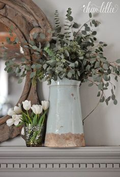 a vase filled with white flowers sitting on top of a mantel next to a mirror