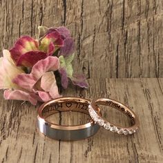 two wedding rings sitting on top of a wooden table next to a bouquet of flowers