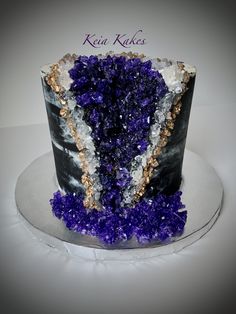 a black and white cake with purple flowers on it's side is decorated with gold accents