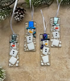 three snowman ornaments hanging from a christmas tree