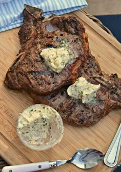 two steaks on a cutting board with some butter and a fork next to it