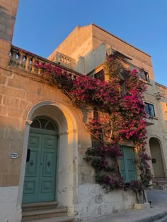 an old building with pink flowers growing on it's side and green doors in front