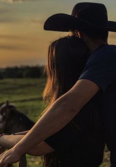 a man and woman standing next to each other in front of a horse at sunset