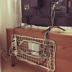 a tv sitting on top of a wooden table next to a window with curtains and wires