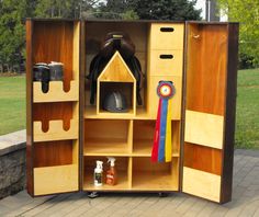 an open wooden cabinet with items inside on the ground near some grass and trees in the background