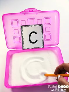 a person is holding a pencil and writing on a pink case with the letter c in it