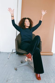 a woman sitting on top of a chair with her arms in the air and smiling