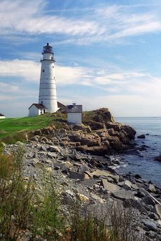 a light house sitting on top of a lush green hillside next to the ocean and rocky shore