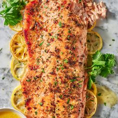 a piece of salmon on a plate with lemons and parsley next to it