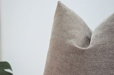 a close up of a pillow on a chair with a plant in the background and a white wall behind it