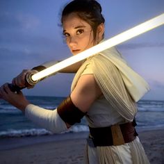 a woman holding a light saber on the beach