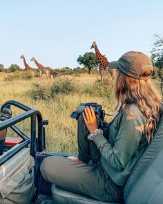 a woman sitting in the back of a truck looking at giraffes