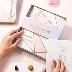 a woman's hands writing on a planner next to two notebooks and flowers