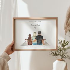 a person holding up a framed photo with their dog and cat on it, in front of a potted plant