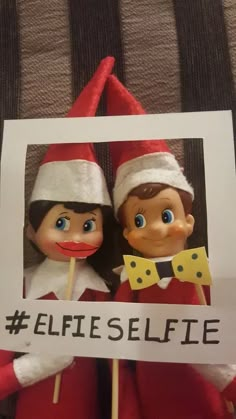 two elfs holding a sign with the words selfie on it in front of them