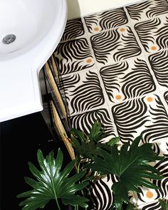 a bathroom with black and white patterned flooring next to a plant on the ground