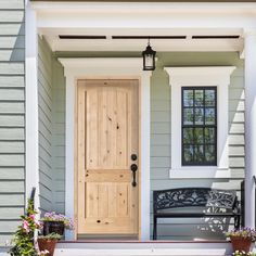 a wooden door sitting on the side of a gray house next to a black bench